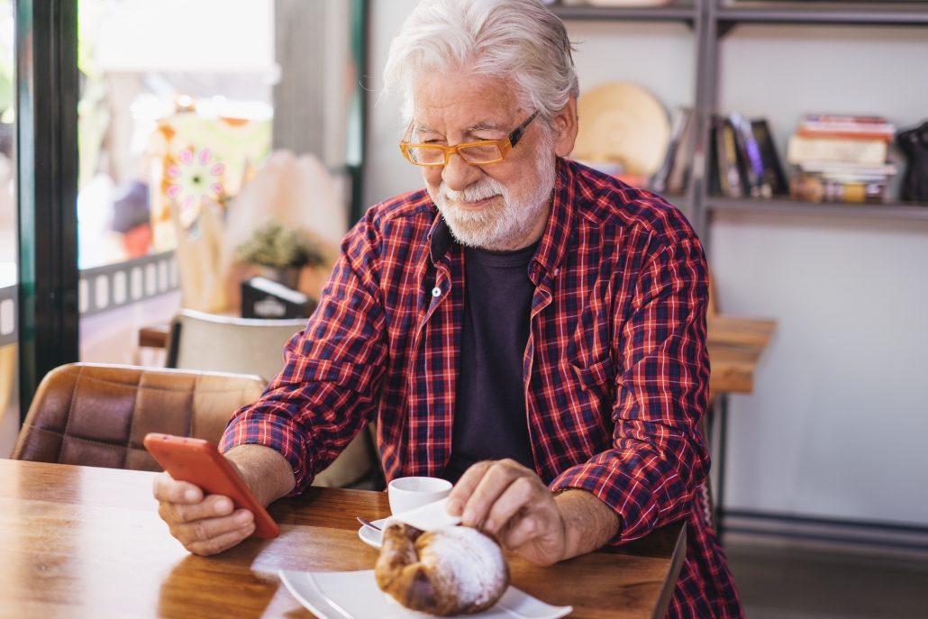 smiling senior bearded man sitting at cafe table using mobile phone